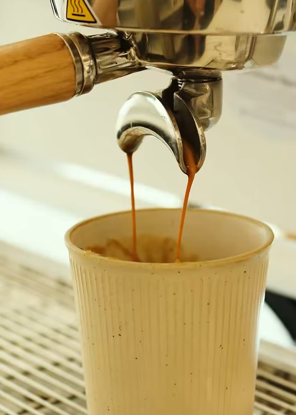 A double shot of espresso streaming into a ribbed ceramic cup.